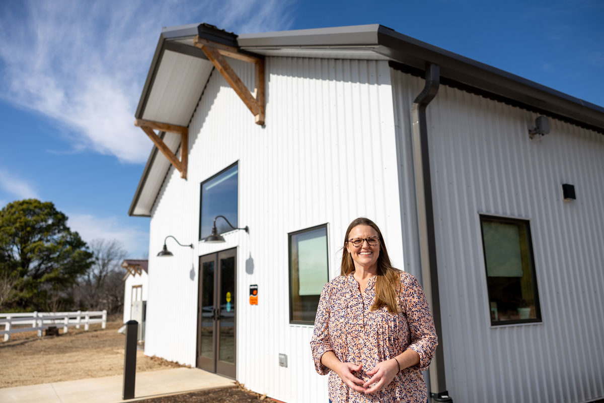 A woman standing in fronf of a white metal building.