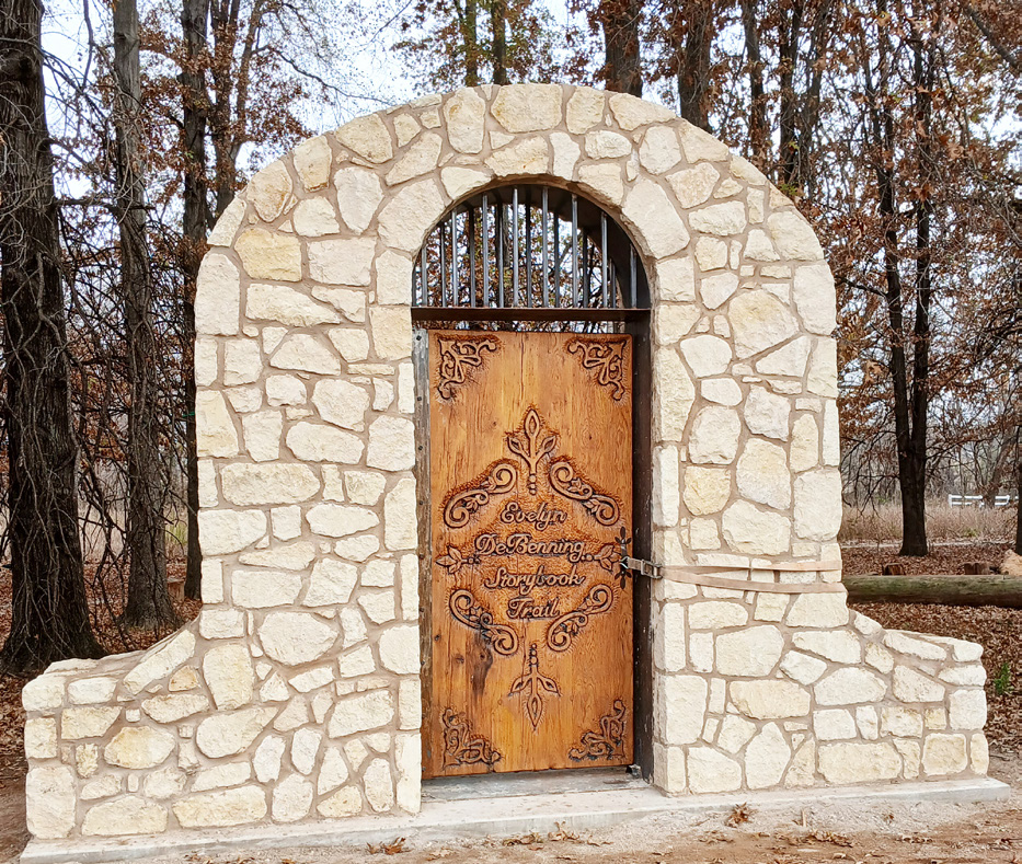 A wooden entry gate that is framed with cobblestone next to an outdoor wooded area.